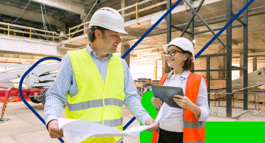 Tecnologia sendo usada na construção. Na imagem um homem e uma mulher, a mulher segurando um tablet e eles estão dentro de uma fábrica.IoT na Construção Civil